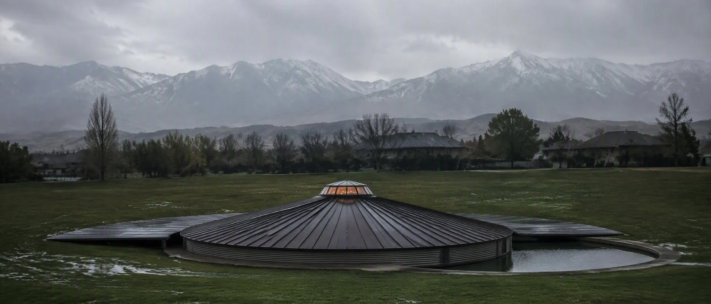 The buried studio at distance on an overcast afternoon, its dark cone low against a wet lawn
