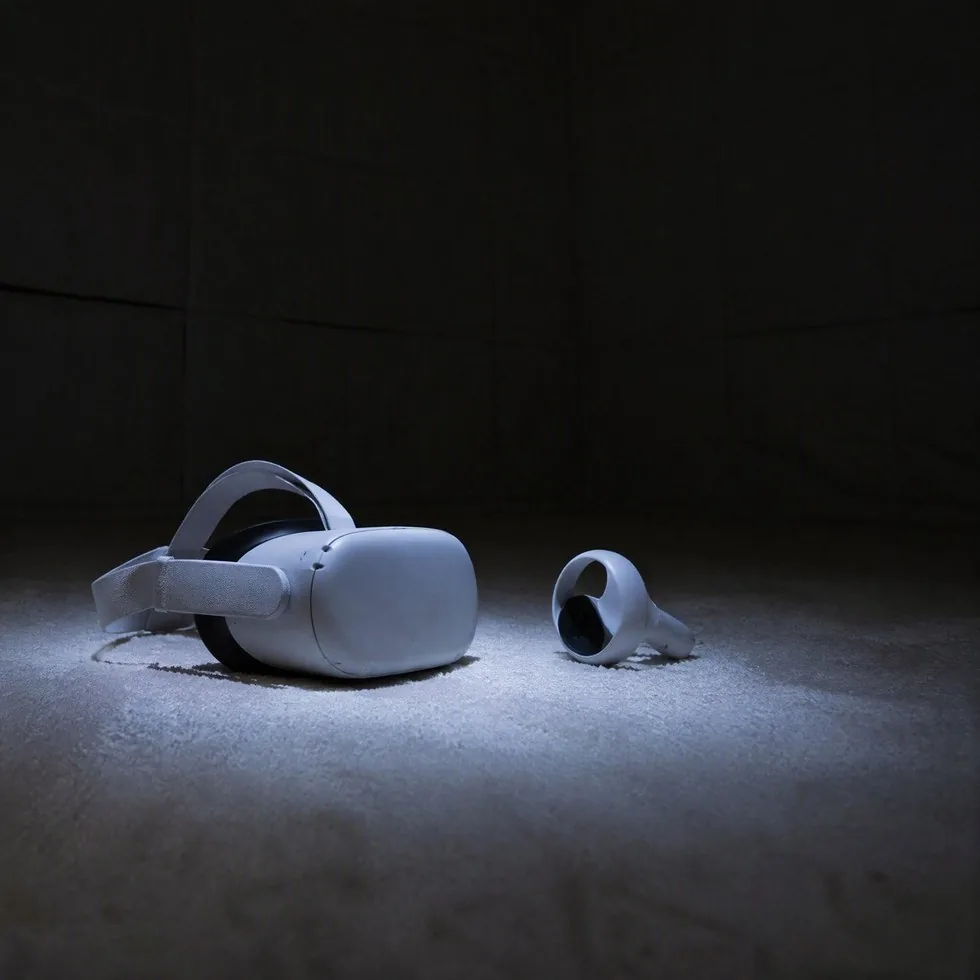 An unbranded white VR headset and one controller set down on the pale floor at the edge of a pool of light